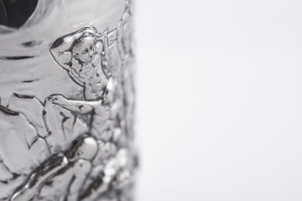 Detail of the Silver champagne bottle cover with bas-relief inspired by mythological bacchanal scene.