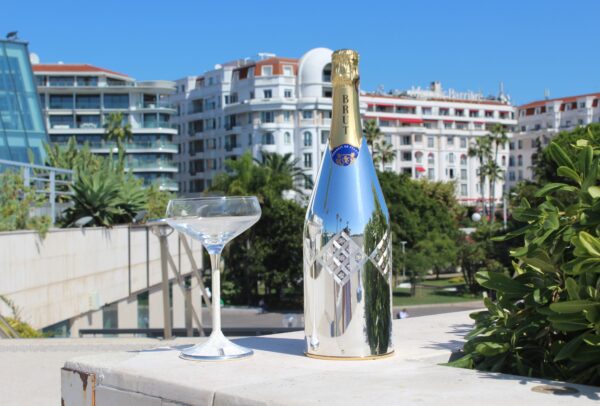 Silver champagne bottle cover with diamond pattern, displayed outdoors with cocktail glass.
