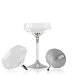 Couple of champagne glasses with a sleek, modern design. The clear glass cup sits atop a slim metal stem, which transitions into a textured, silver-finished base featuring a small plaque engraved with the word 'KOVER'.