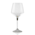 Single wine glass with a sleek, modern design. The clear glass cup sits atop a slim metal stem, which transitions into a textured, silver-finished base featuring a small plaque engraved with the word 'K-OVER'.