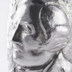 Artistic silver champagne bottle cover, finely engraved with expressive human faces emerging from textured surfaces, creating a sculptural effect that blends contemporary design and traditional craftsmanship.