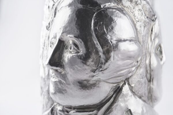 Artistic silver champagne bottle cover, finely engraved with expressive human faces emerging from textured surfaces, creating a sculptural effect that blends contemporary design and traditional craftsmanship.