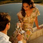 elegant sunset scene of a couple toasting on the edge of a swimming pool with wine glasses filled with white wine