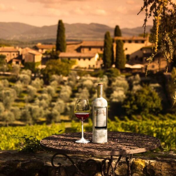 Tuscan landscape in the background. in the foreground a glass of red wine and a silver wine bottle cover